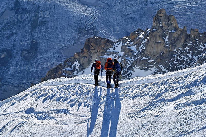 Three ascended mountaineers run across a snow-covered mountain ridge, Aiguille du Midi, Chamonix-Mont-Blanc, Haute-Savoie, France