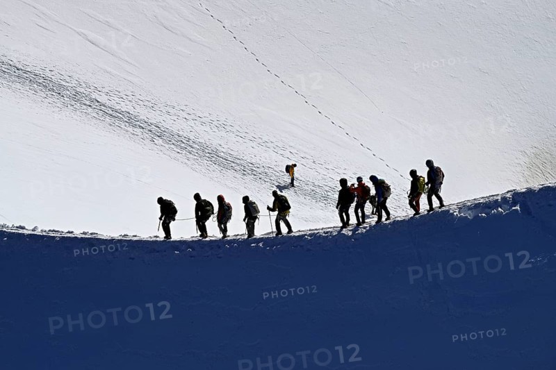A group of mountaineers runs across a snow-covered mountain ridge, Aiguille du Midi, Chamonix-Mont-Blanc, Haute-Savoie, France
