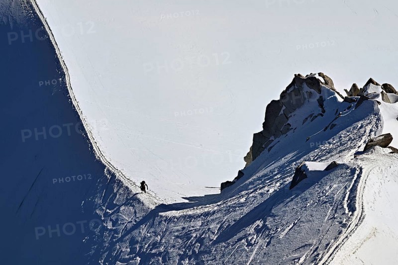 A mountaineer climbs over a snow-covered mountain ridge, Aiguille du Midi, Chamonix-Mont-Blanc, Haute-Savoie, France