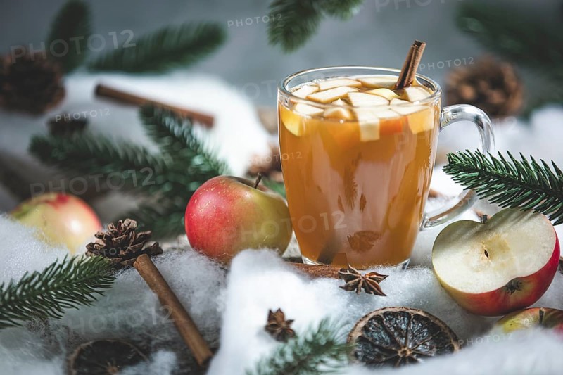 A glass of apple punch and apple pieces in a wintery setting