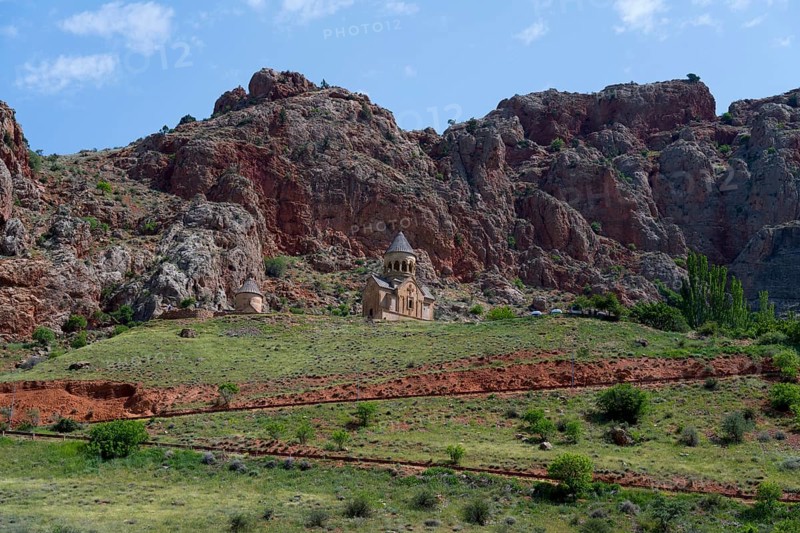 Church on green meadow against dramatic rocky backdrop under blue sky, Noravank monastery, Surb Astvatsatsin mausoleum church and Surb Karapet baptism church, Noravank, Vayots Dzor province, Wajoz Dzor, Armenia, Caucasus