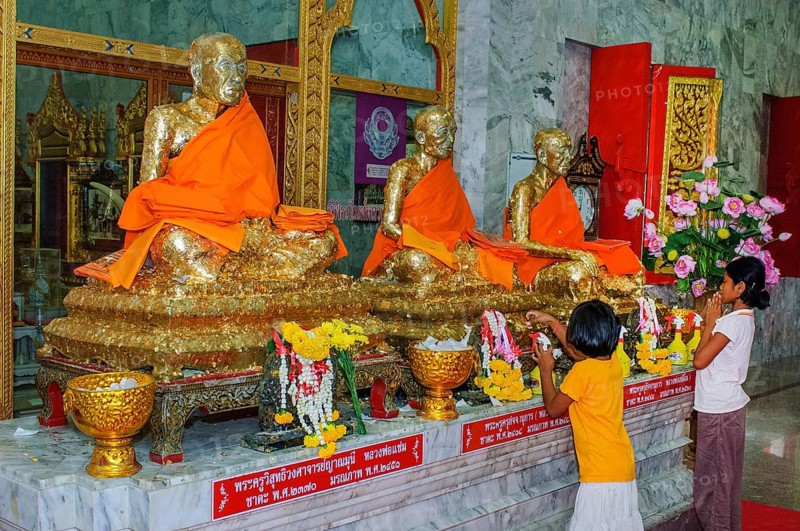 Buddhist believers Buddhists pray making offerings to statues of Buddhist monks covered with gold leaf at Wat Chalong Monastery, Phuket Island, Phuket Province, Thailand