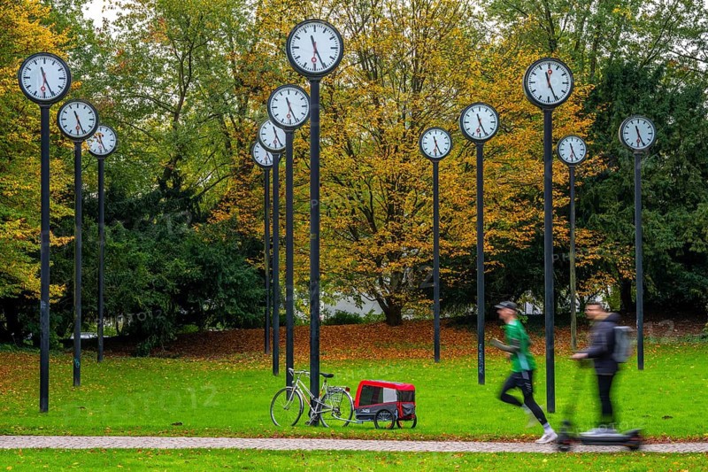 The art installation Zeitfeld in Volksgarten Park in Düsseldorf-Oberbilk, a total of 24 station clocks, on 6 meter high steel columns, have been running synchronously since 1987, jogger in the municipal park, artwork by Düsseldorf artist Klaus Rinke, symbol of time, time change, North Rhine-Westphalia, Germany