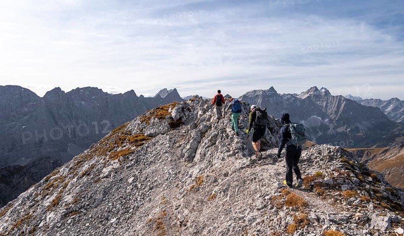 Hikers on the summit ridge of the Gamsjoch, behind rock faces of the Laliderer Spitze, eastern Karwendel, Tyrol, Austria