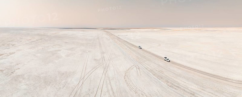 Aerial view, two off-road cars driving on a salt pan, arid landscape, Botswana