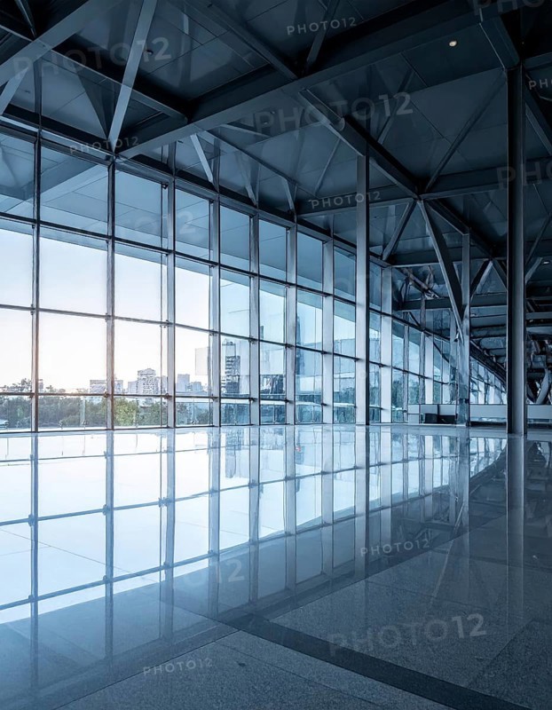Modern architectural framework with glass and steel structure, glass facade with a greed of steel arrows, blue sky with a soft golden light of a sunrise, AI generated
