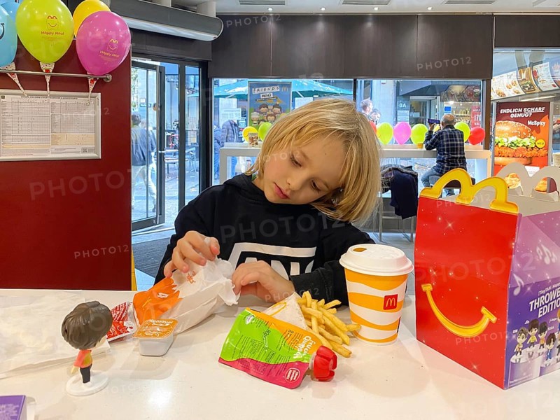Interior view, child, boy, 7 years, blonde, eating Happy Meal, children's menu, at McDonald's restaurant, drink, French fries, balloons, logo, Stuttgart, Baden-Württemberg, Germany