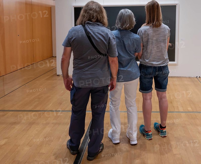 Three visitors look at a painting in an exhibition, Bavaria, Germany