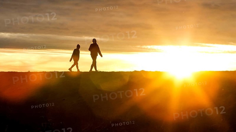 Woman and child walk across a dike on the island of Fehmarn at sunset, 13.10.2025, Fehmarn, Schleswig-Holstein, Germany