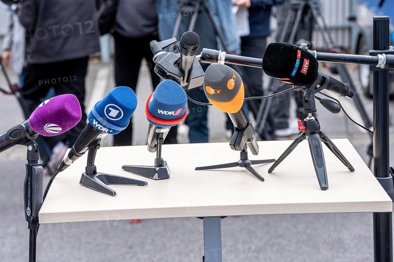 Microphones from various radio stations, television stations, standing on the table, at a press conference