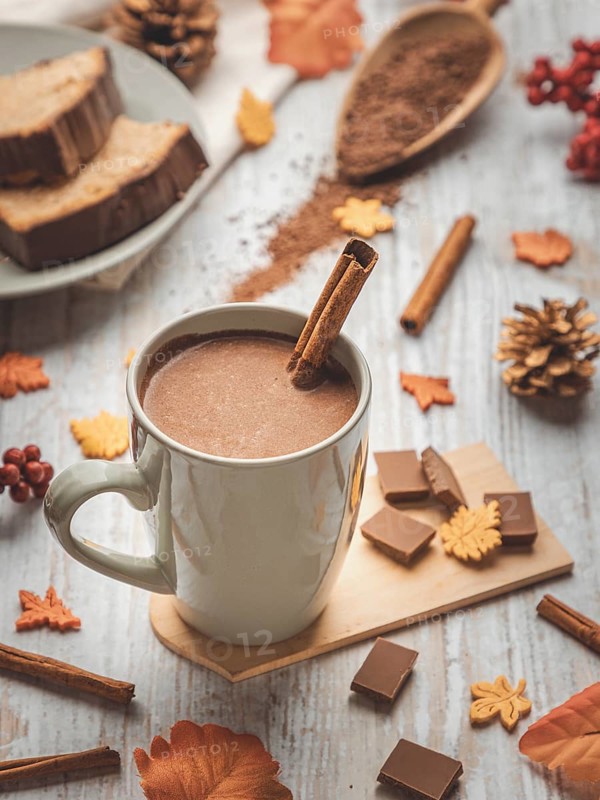 A cup of hot chocolate with cinnamon sticks, cake and autumn decorations