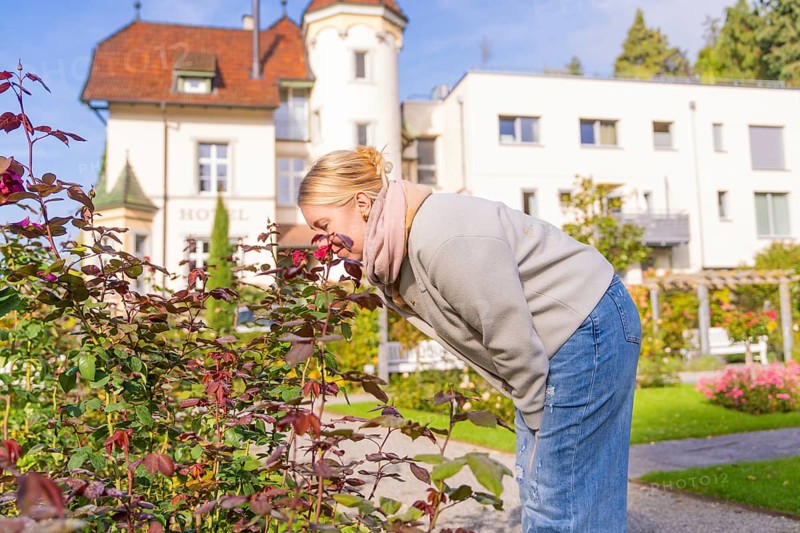 Woman smells of flowers in a sunny garden in front of a house, Überlingen, Lake Constance, Germany