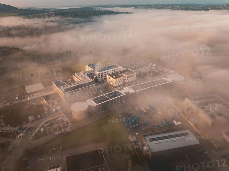Building in an industrial area seen from above in fog, surrounded by landscape at daybreak, new hospital health campus building, Calw, Germany