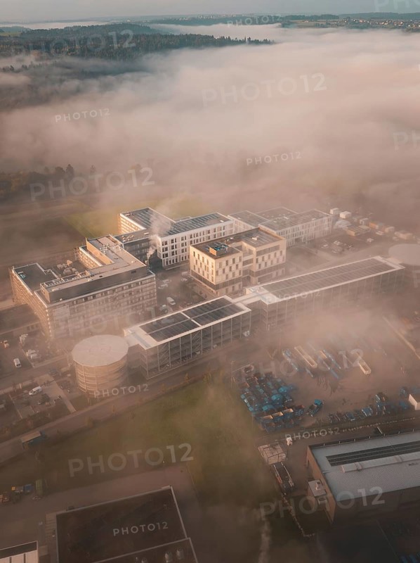 Aerial view of a complex of buildings in thick morning fog, modernly embedded in a natural landscape, new hospital health campus building, Calw, Germany