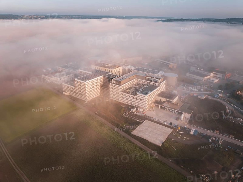 Industrial buildings seen from the air in morning fog, surrounded by natural landscape at dusk, new hospital health campus building, Calw, Germany