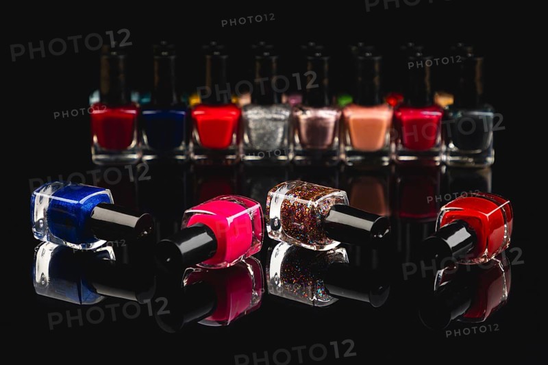 Different nail polish bottles in intense colors on a black surface with reflection