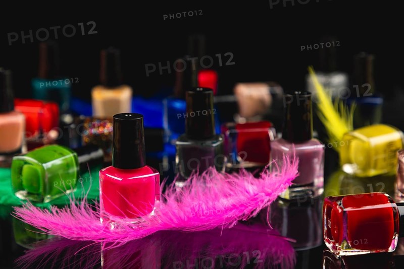 Colourful nail polish bottles and coloured feathers on black surface with reflection