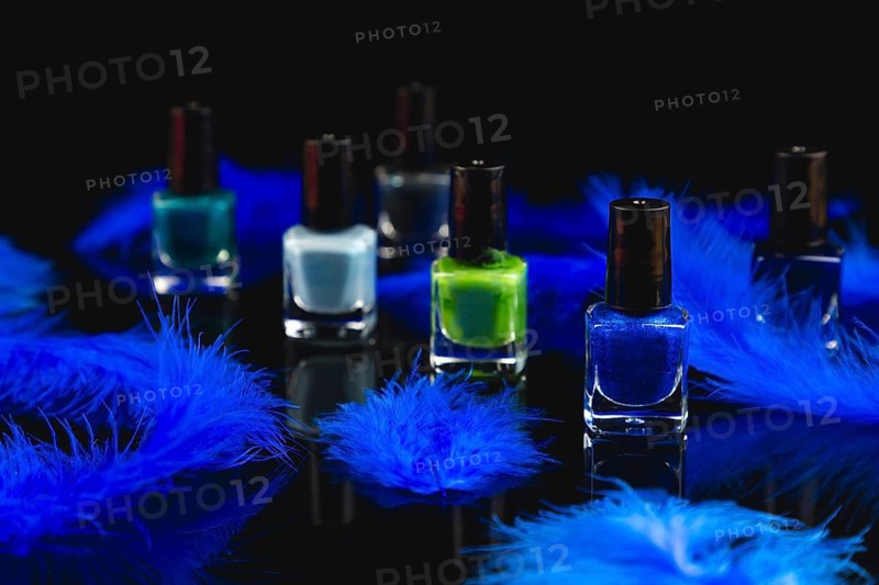 Nail polish bottles in shades of blue and green with blue feathers on a black surface with reflection