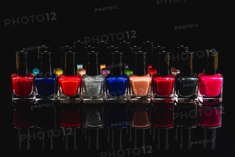 A variety of nail polish bottles in different colors with reflections on a black background