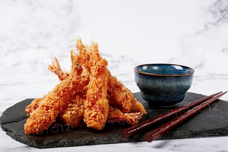 Shrimp in tempura, deep fried, on black slate, with sauce, light marble table, no people