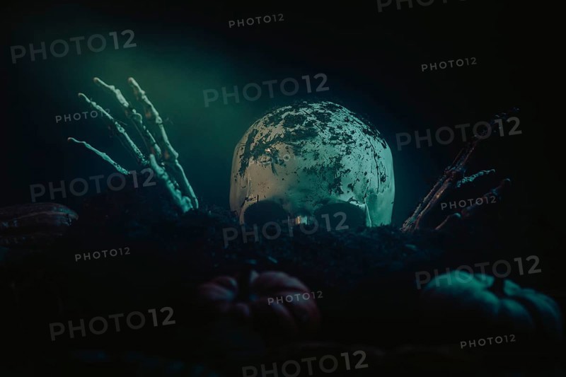 Halloween scene with a skull, skeletonised hands and pumpkins in dark earth
