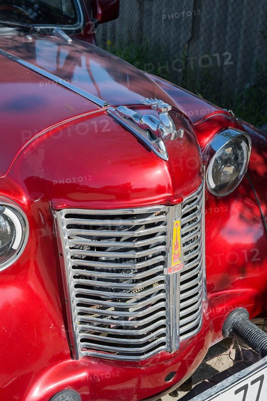 Front of a shiny red vintage car with a striking emblem in the sun, Moskvich 401, Armavir province, Armenia