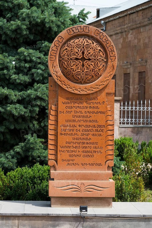 An elaborately engraved stone khachkar with complex ornaments and Armenian characters, surrounded by trees and plants, Khachkar, cross stone, Aghavnatun, Armavir province, Armenia