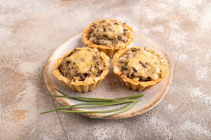 Tartlets with meat and cheese on brown concrete background. side view, close up
