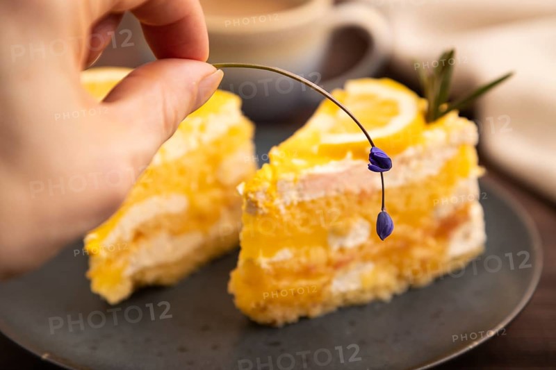 Lemon cake with hand on brown wooden background and linen textile, cup of coffee, side view, close up, selective focus