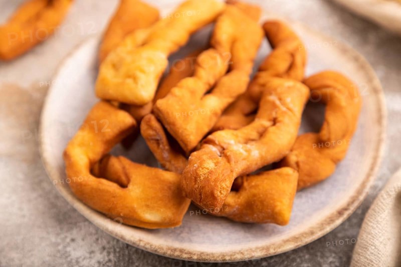 Crunchy biscuit Brushwood cookies sprinkled with powdered sugar on brown concrete background and linen textile, cup of coffee, side view, selective focus
