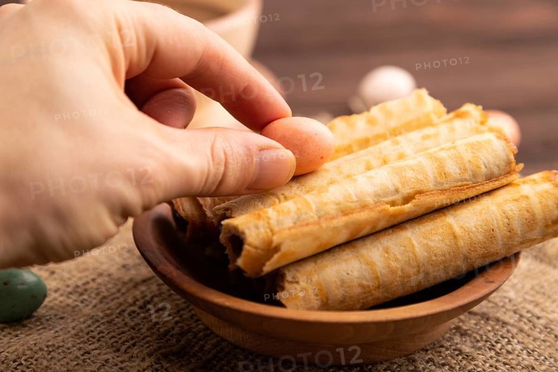 Waffles with caramel with hand on brown wooden background and linen textile, cup of coffee, side view, selective focus