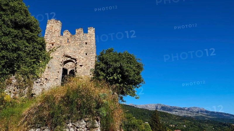 Ancient ruined tower with neighbouring trees against a picturesque blue sky and mountain backdrop, Mystras, Mistra, UNESCO World Heritage Site, Medieval Byzantine ruined city, northwest of Sparta, foothills of the Tyagetos Mountains, Peloponnese, peninsula, Greece