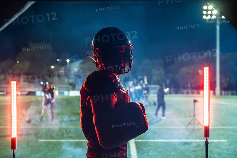 American football player in full gear holding a ball, standing confidently on a floodlit stadium field at night, intensely focusing on the upcoming game or practice