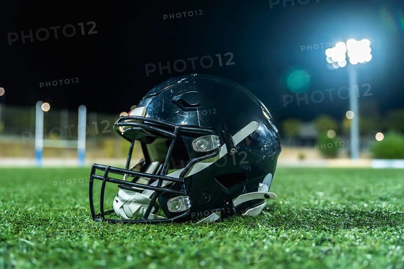 American football helmet lying on green artificial turf field with goal posts and bright stadium lights illuminating the arena at night, representing competition and sports
