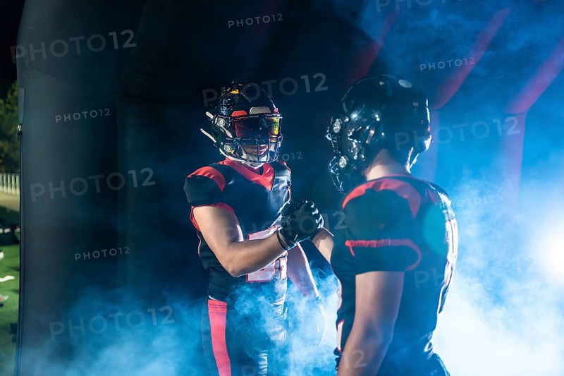 American football players wearing uniforms and helmets shaking hands, showing sportsmanship and teamwork as they prepare to enter the field through a smoky tunnel