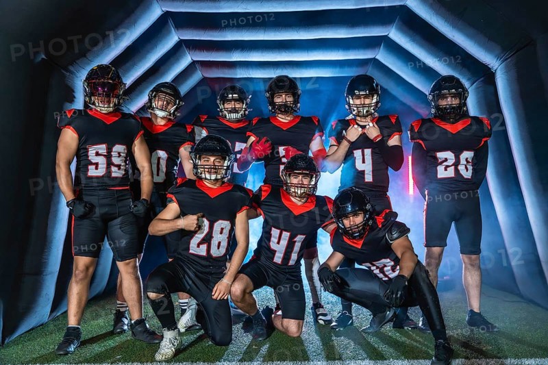 American football team players in uniforms and helmets posing together inside a stadium inflatable tunnel, preparing for a game with determination and confidence