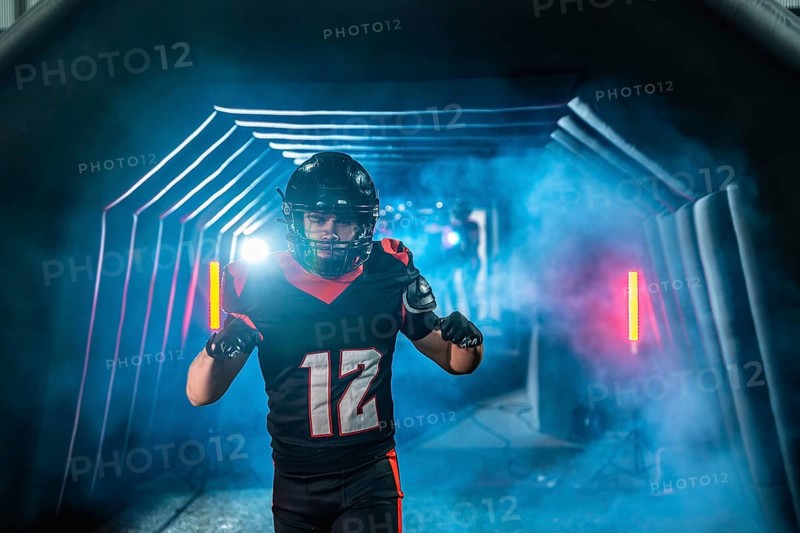 American football player with helmet and uniform running from a smoky tunnel with blue and red lights, creating a dramatic entrance at a sports stadium