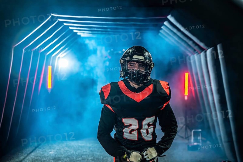 American football player in uniform and helmet emerges from a fog filled stadium tunnel into dramatic spotlight, ready and focused to take the field for the big game