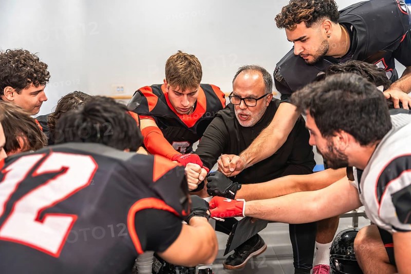 American football coach and players huddling in a locker room, getting motivated for a game while placing their fists together in a gesture of unity and teamwork
