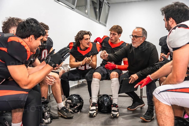 American football coach briefing players in a locker room, outlining strategy and motivating the team before or during the game, focused leadership and determined preparation
