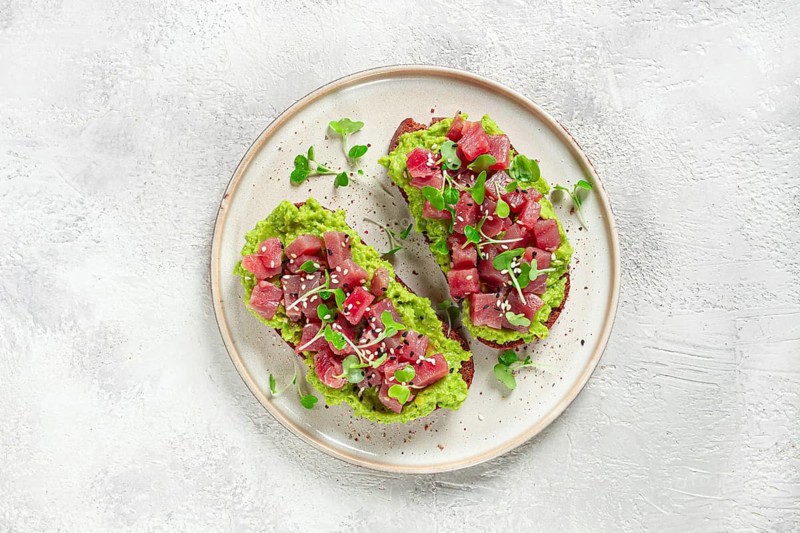 Toasts with fresh tuna and avocado, spread on black bread and sprinkled with microgreens, breakfast, healthy food
