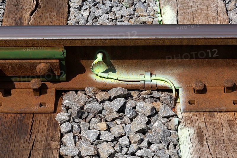 Close-up of ballast and bright green fluorescent spray painted metal ground wire attached to rusted railway track, Quebec, Canada
