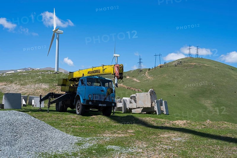 A blue crane lorry stands on a green construction site next to a wind turbine on a hill, Pushkin Pass, Lorikeet Province, Bazum Mountains, Lesser Caucasus, Armenia