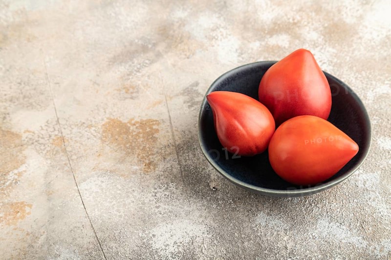 Red Heart shape tomatoes in blue bowl on brown concrete background. Side view, copy space. healthy food, vegetable, minimalism
