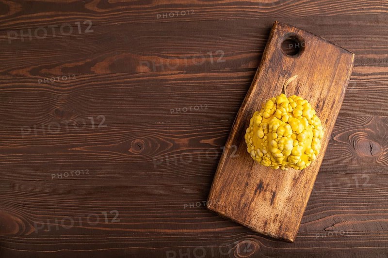 Decorative orange Pumpkin with tumors on cutting board on brown wooden background, top view, flat lay, copy space, minimalism