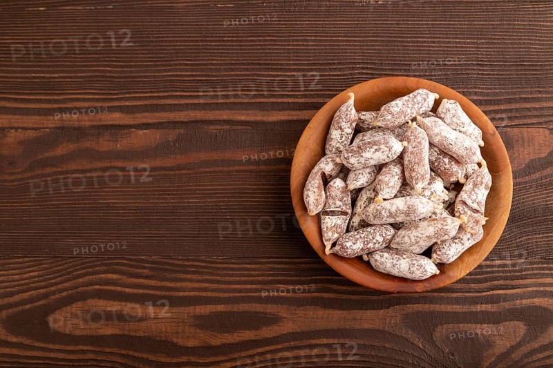 Small smoked Chicken sausages in wooden bowl on brown wooden background. top view, flat lay, copy space