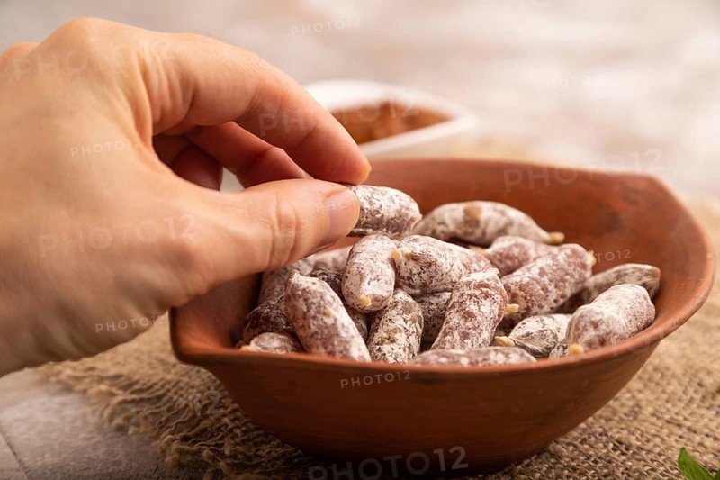 Small smoked Chicken sausages in clay bowl with hand on brown concrete background and linen textile. side view, close up, selective focus