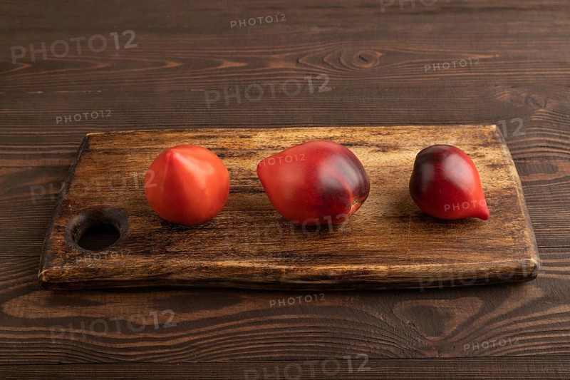 Red Heart shape tomatoes on cutting board on brown wooden background. Side view, copy space. healthy food, vegetable, minimalism