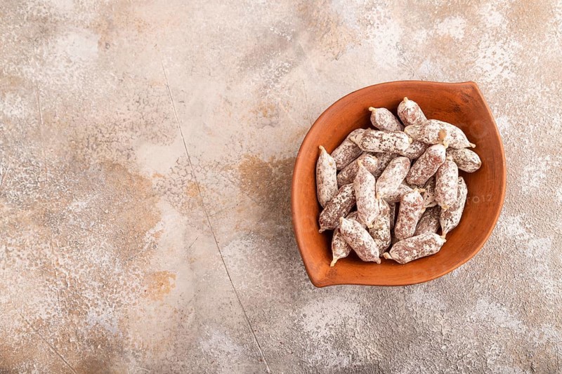 Small smoked Chicken sausages in clay bowl on brown concrete background. top view, copy space