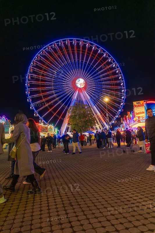 Colourful Ferris wheel lights up the night, surrounded by visitors in a festive atmosphere, Cannstatter Wasen funfair, Stuttgart, Germany